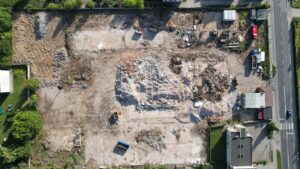 Plac budowy z lotu ptaka, hałda gruzu w centrum, sprzęt budowlany, budynek w rogu posesji; inspekcja obiektu z drona VisDron